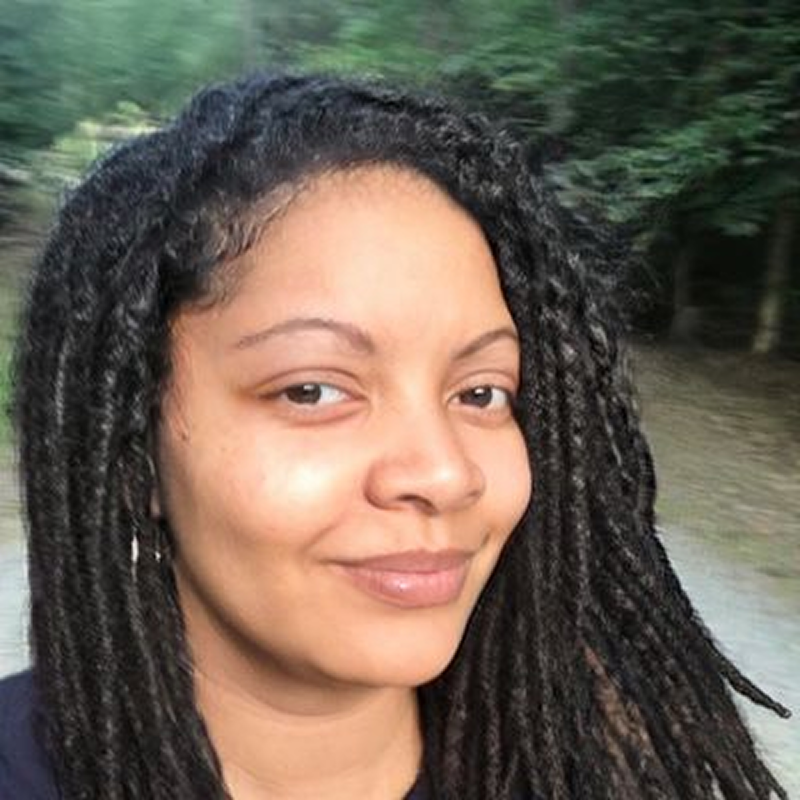 Smiling woman with long braided hair outdoors.